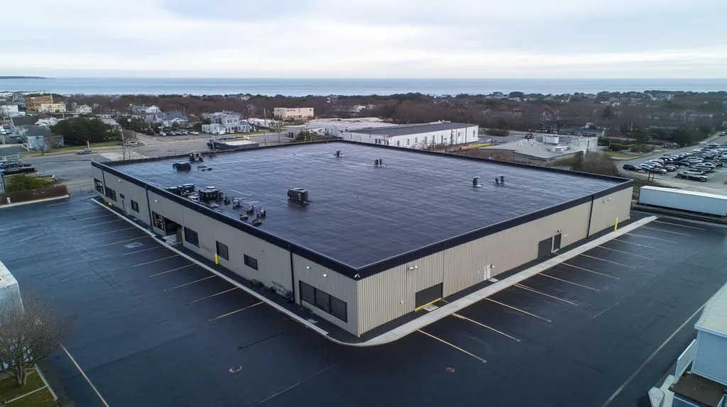 A commercial roof on a warehouse in a location similar to Newport, Rhode Island with a rainy day aesthetic (AI image)