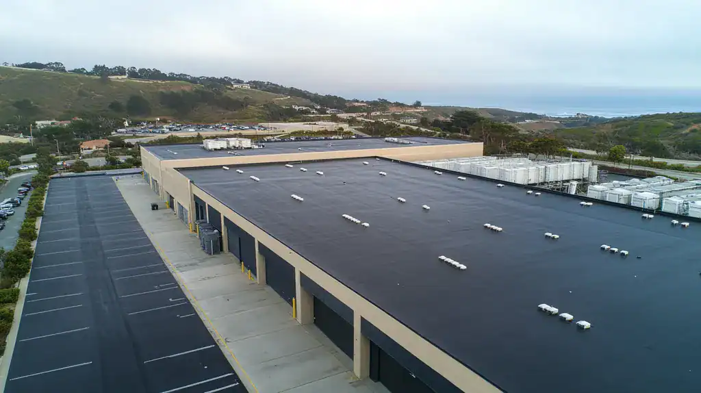 A commercial roof on a distribution center in a location similar to Big Sur with a rainy day aesthetic (AI image)