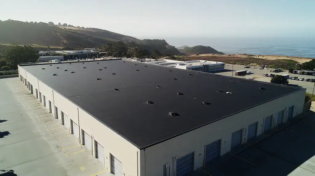 A commercial roof on a warehouse in a location similar to Big Sur with a color highlight aesthetic (AI image)